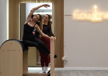 Instrutora de Pilates ajudando uma aluna a fazer um alongamento lateral no ladder barreldel