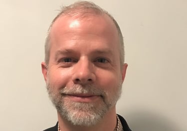 Alexander Slagg with grey beard, black sport coat, checkered button down shirt