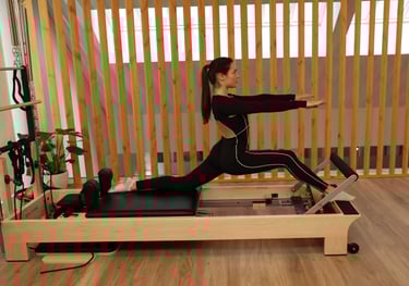 Uma mulher a realizar um alongamento em abertura no reformer num estúdio moderno 