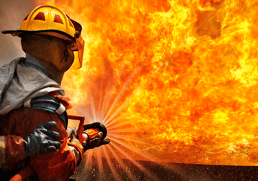 Um bombeiro combate um grande incêndio com uma mangueira, exemplificando uma crise.