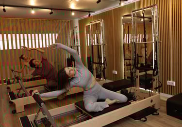 Three people performing a side stretch on reformers in a Pilates studio with wooden accents 