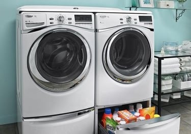 Front-loading washer and dryer in a laundry room with a storage drawer containing detergent and cleaning supplies underneath.