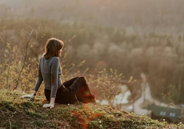 a woman sitting on a hill with a dog