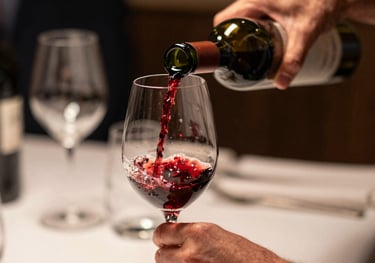 Close-up of a sommelier's hands carefully pouring red wine into a glass in a dimly lit, high-end South American establishment. Focus on the wine's texture and the elegant movement.