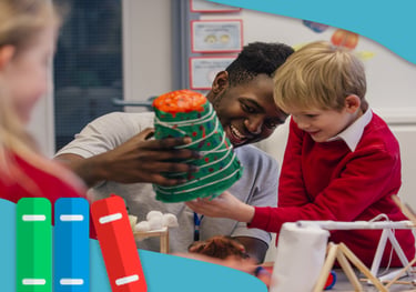 Smiling teacher helps elementary student with a colorful science volcano project in a classroom.