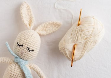Amigurumi de crochet en forma de conejo color beige con madeja de estambre y gancho