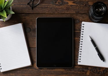 A top-down view of a stylish Latin American workspace with a tablet, a clean notebook, and a small plant, illustrating organization and modern business management.