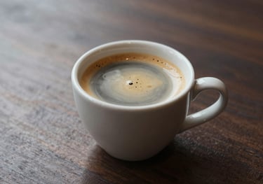 A refined shot of a coffee cup with perfect crema on a dark wood table #2A1A10, with soft lighting highlighting the quality of the brew.