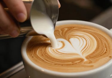 Macro shot of a barista's hand pouring steamed milk into a ceramic cup to create a heart shape, warm brown and cream tones, premium style.