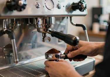 Professional photography of a silver espresso machine in a modern North American / US cafe, with a barista's hands carefully tamping fresh grounds, deep brown tones.