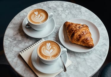 A top-down view of a marble coffee table in a North American / US cafe featuring a latte, a croissant, and a notebook, styled with elegance and natural materials.