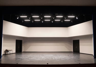 A wide shot of a contemporary theater stage at George Mason University in North American / US, during a rehearsal with dramatic navy and white lighting.