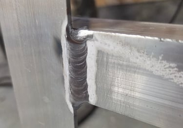 Close-up of an aluminum weld joint on aluminum square tube angle in a metal fabrication workshop.