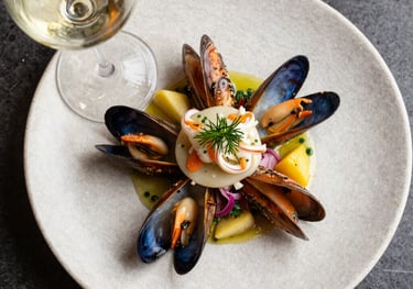 A top-down shot of a gourmet seafood dish paired with a glass of crisp white wine. Modern Spanish plating style on a stone-textured plate. Natural, bright lighting.