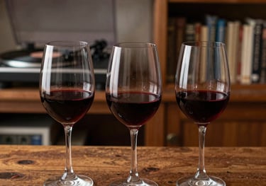 Three glasses of red wine lined up on a bar made of aged wood. In the blurred background, a vinyl record player and shelves of books create a warm, intellectual atmosphere typical of a Spanish study.