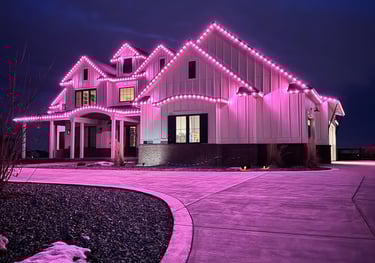 Modern white farmhouse decorated with vibrant pink exterior LED holiday trim lighting at night.