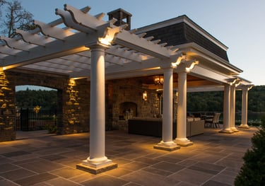 Luxury outdoor patio featuring a white pergola with stone pillars and integrated lighting at sunset.