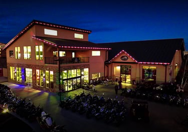 Motorcycle dealership showroom at night with rows of bikes and colorful holiday lights.