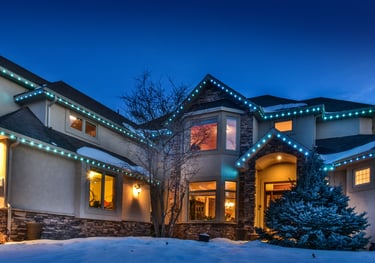 Luxury home exterior with festive blue LED Christmas lights on the roofline during winter twilight.
