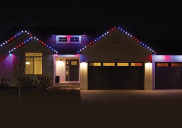 Modern white house at night with festive red, white, and blue permanent LED holiday roof lighting.