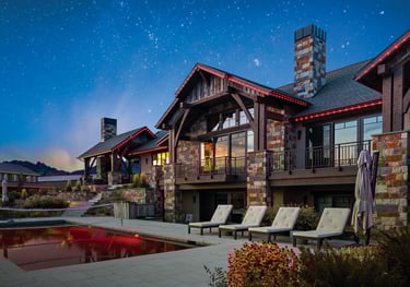 Luxury mountain estate with stone exterior, pool, and lounge chairs under a starry night sky.