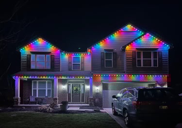 Two-story suburban home decorated with vibrant rainbow LED Christmas lights at night.