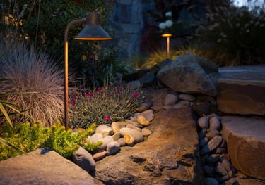 Warm outdoor lighting illuminates a stone pathway and garden plants, enhancing the nighttime landscape design.