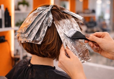 Professional stylist applying hair highlights using foil and a brush at a hair salon.