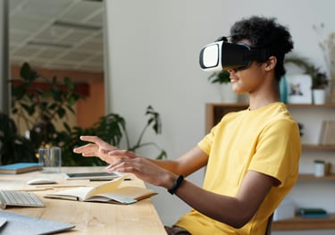 Lifestyle image of a student wearing VR headset, yellow t-shirt, and sitting at a cluttered desk.