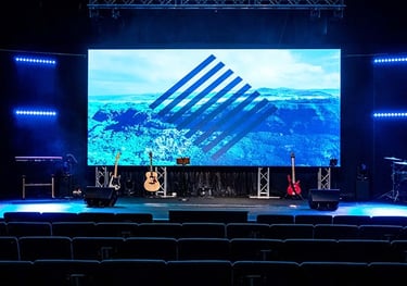 Professional concert stage with a large LED video wall and musical instruments under blue lighting.