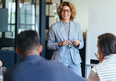 Smiling female business executive in a grey suit leading a corporate meeting or workshop.