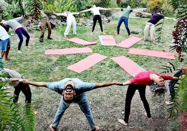A diverse group of people performing a circle yoga stretch outdoors on green grass with pink mats.