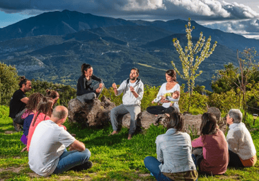A group of people sitting in a circle on a grassy mountain hill for an outdoor wellness retreat.