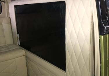 Uma TV de tela plana embutida em um painel creme claro customizado no interior da Kombi.