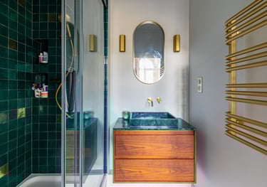 Modern bathroom with green tiles, wood vanity, gold fixtures, and a heated towel rack.