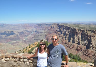 a man and woman standing on a cliff overlooking the grand canyon