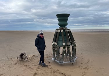 Tracey Billington standing by the time and tide bell on mablethorpe beach