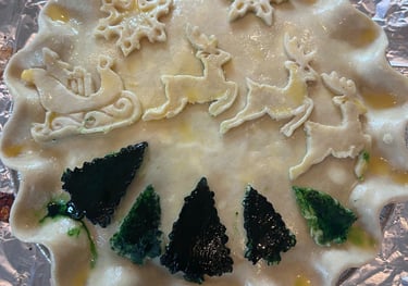 A festive homemade Christmas pie crust decorated with dough reindeer, sleigh, and green trees.