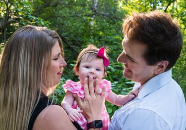 A happy couple holding the child and gazing at her. The child glances at the camera, smiling slightly. 
