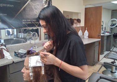 A cosmetology student applying hair foil highlights to a client at a professional barber school.