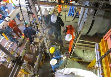 Offshore oil rig workers performing heavy industrial maintenance and equipment inspection on a metal platform.
