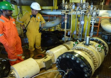 Oil and gas engineers in coveralls inspecting industrial pipeline valves on an offshore platform.