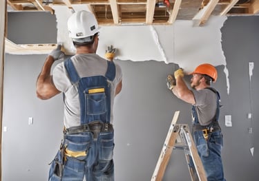 Two men in overalls repairing a ceiling.