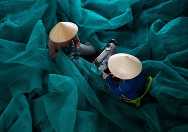 Two women wearing traditional Vietnamese conical hats repairing a fishing net.