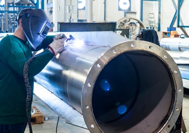 a man in a welding helmet welding a stainless steel pipe