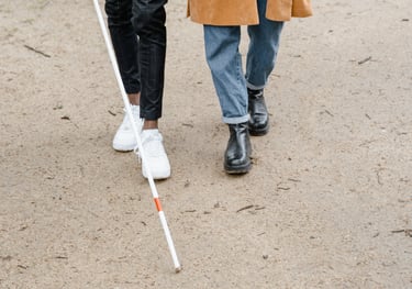 Un homme mal voyant avec sa canne accompagné d' une aidante marchant sur un chemin