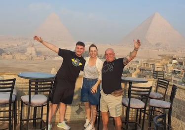 Foto de família de turistas do Brasil na varanda de um hotel em Gizé, observando o complexo das Pirâmides e a Grande Esfinge 