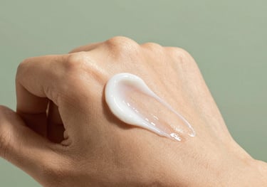 Macro photography of a silky skincare cream being applied to healthy skin, capturing texture and a sense of luxury against a sage green background.