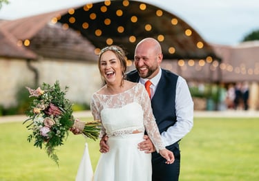 Bride and groom laughing outside Old Gore barn wedding venue in the Cotswolds, captured candidly by photographer Owen Mathias