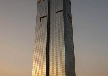 Sleek, modern commercial skyscraper in Gurgaon during sunset. The clean glass exterior reflecting warm gold and dark charcoal hues of the sky. Elite wealth creation aesthetic, prestigious and highly secure atmosphere, real estate photography.